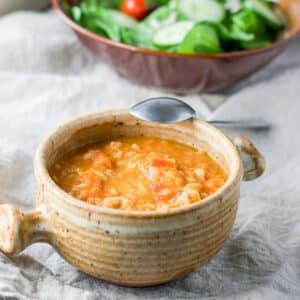 The bean soup in a crock with a spoon leaning on it and a salad in the background - square