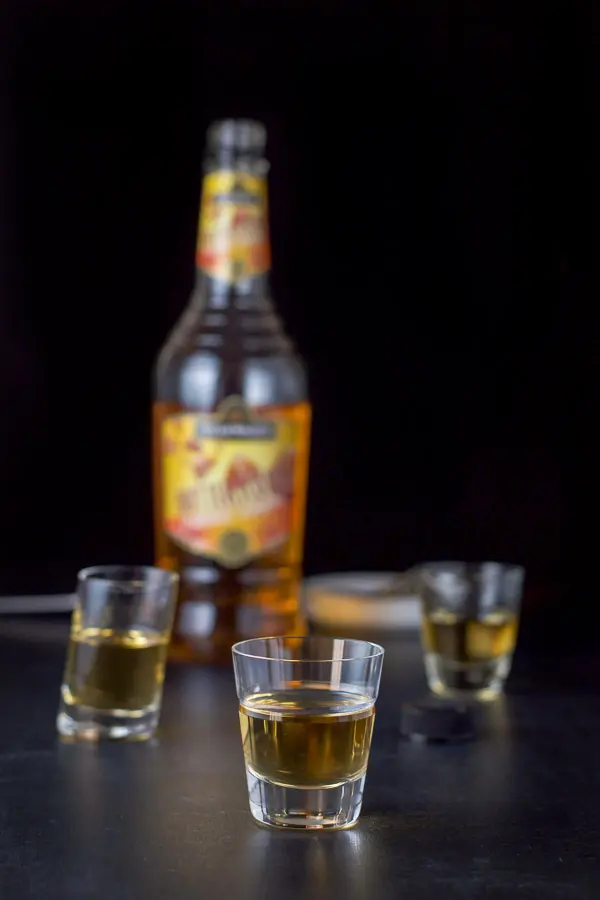 Butterscotch schnapps poured out in the three shot glasses with the bottle in the background