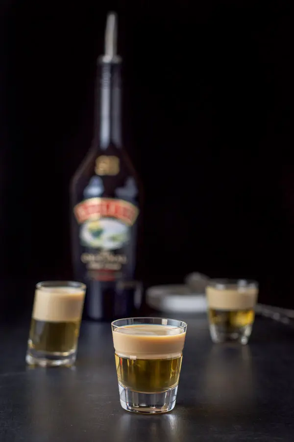 Baileys Irish cream layered in the three glasses with the bottle, pourer and spoons in the background
