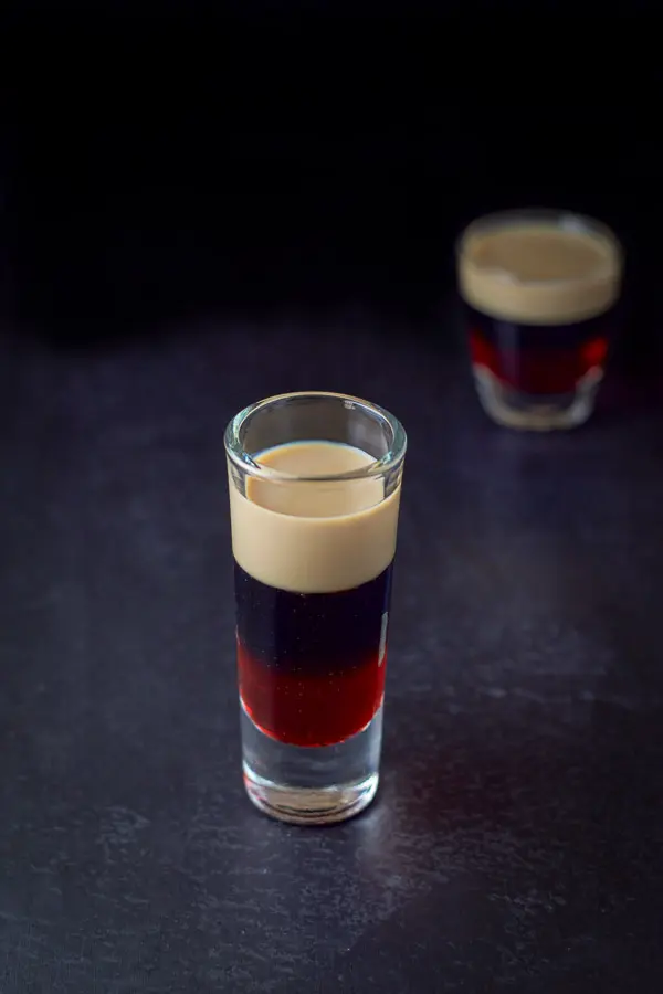 A clear view of the top of the glass of baileys, kahlua and grenadine, the tall glass in front of the shorter glass