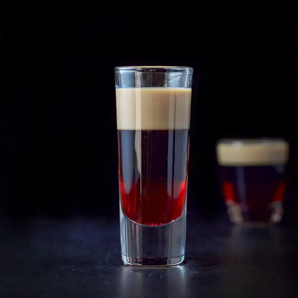 Tall glass of filled with the layered shot and shorter glass in the background