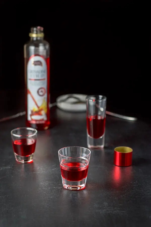 Grenadine poured into the three shot glasses with the bottle and spoons in the background