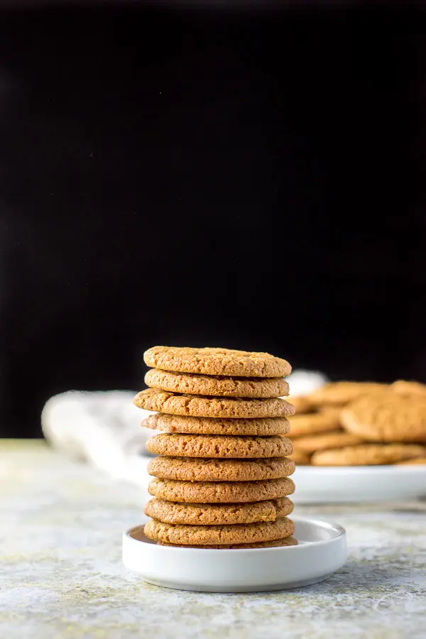 Tower of molasses cookies in a small white plate with more cookies in the background