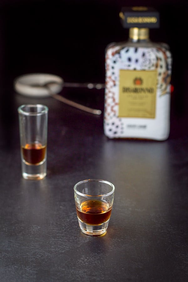Amaretto poured into the glasses with the bottle and cocktail spoon in the background