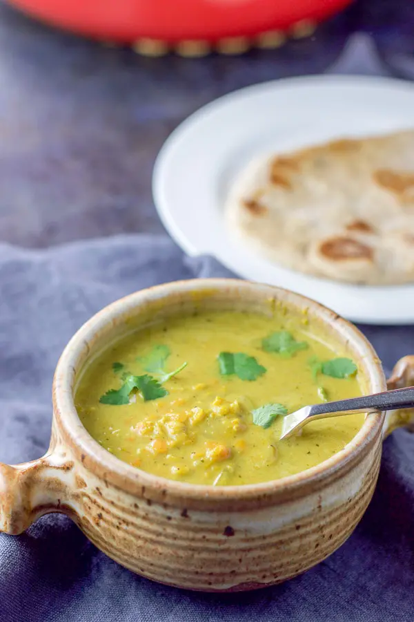 A close up view of the coconut lentil soup in a crock and some naan behind it
