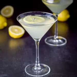 The classic martini filled with the lemon martini with lemon wheels floating in it and lemons on the table