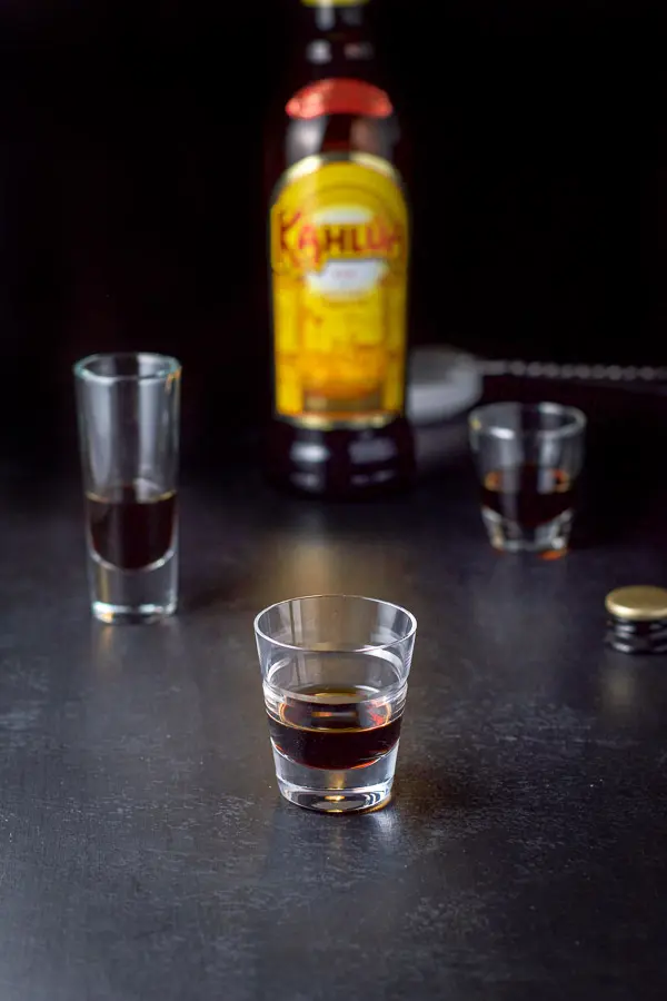 Kahlua poured out in the three shot glasses with the bottle in the background