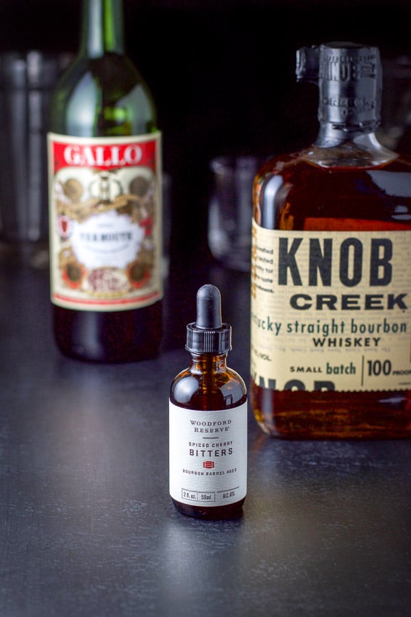 Bitters, bourbon, sweet vermouth for on a table with the shaker in the background