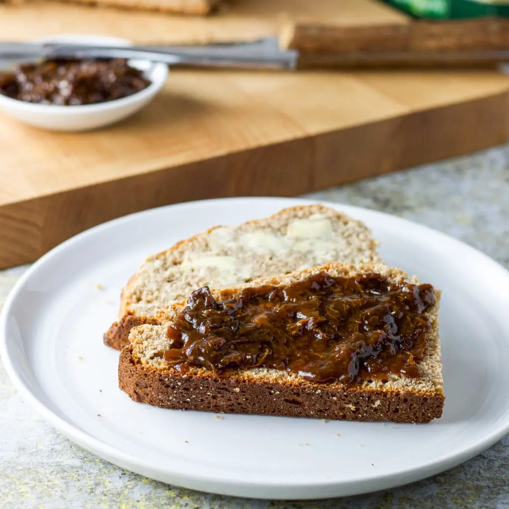 Two pieces of bread, one with prune spread the other with butter in front of a cutting board and knife