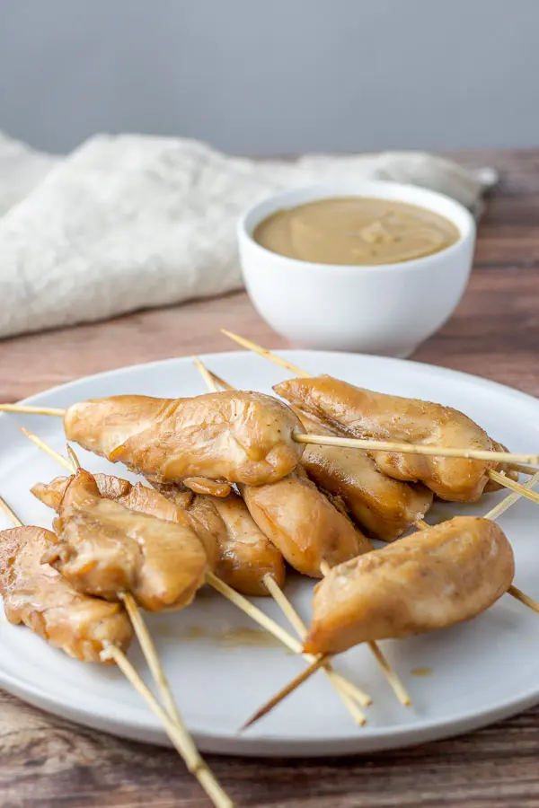 Freshly baked chicken on skewers with peanut sauce in the background