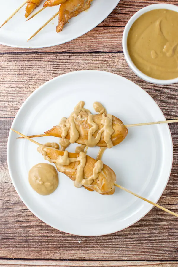 Overhead shot of the chicken satay on a white plate with peanut sauce drizzled on