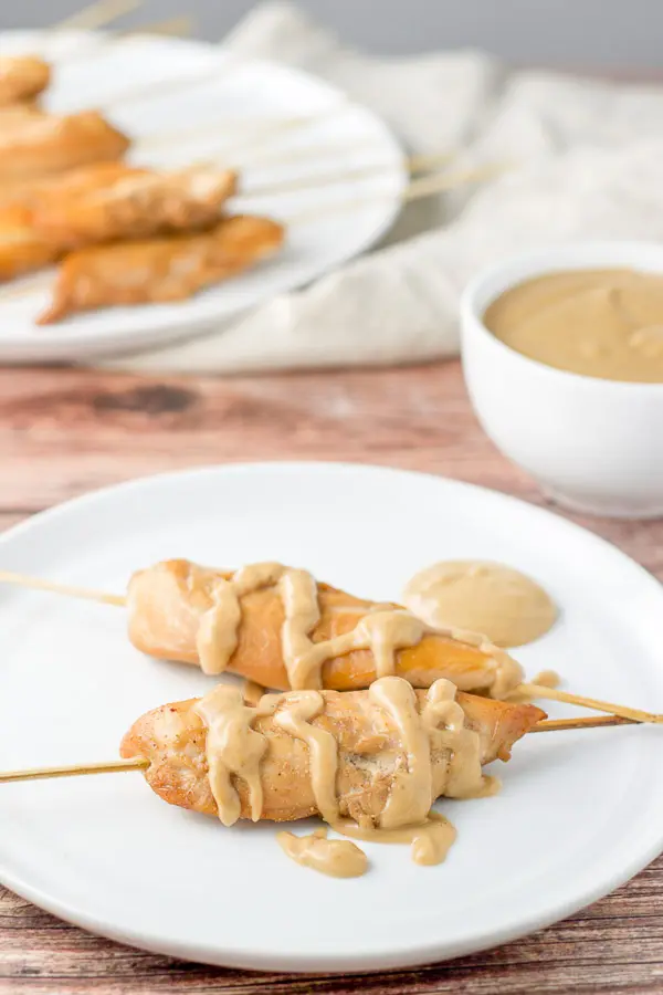 Close up of the satay with peanut sauce on it. There is also a bowl of sauce and more skewers in the background