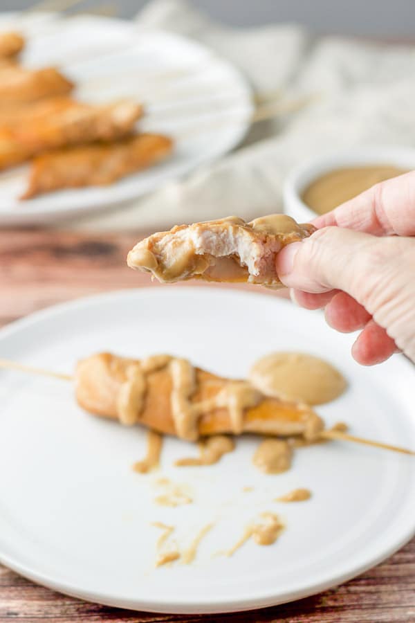 A female hand holding a piece of chicken with a bite taken out of it