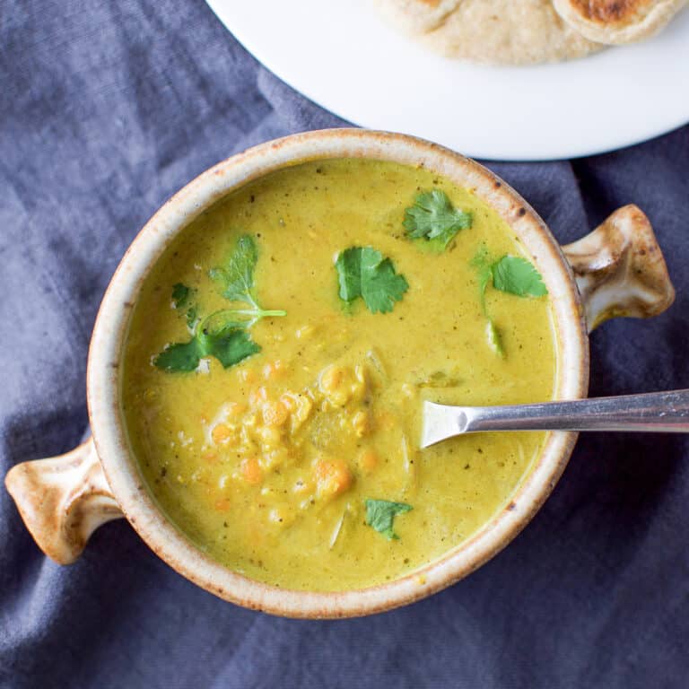 Overhead view of a crock of soup with fresh parsley floating and a sliver of naan bread in the upper right
