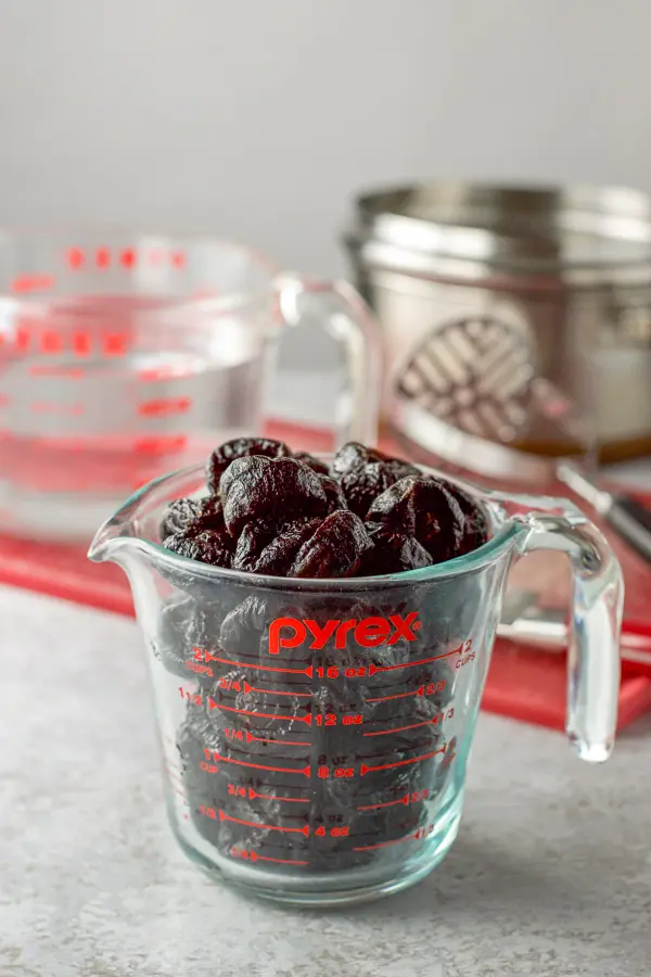 Prunes in a measuring cup with another cup with water and the pan in the background