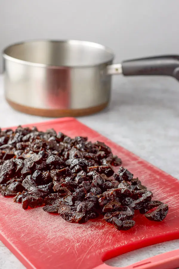 Cut up prunes on a red cutting board and a pan in the background