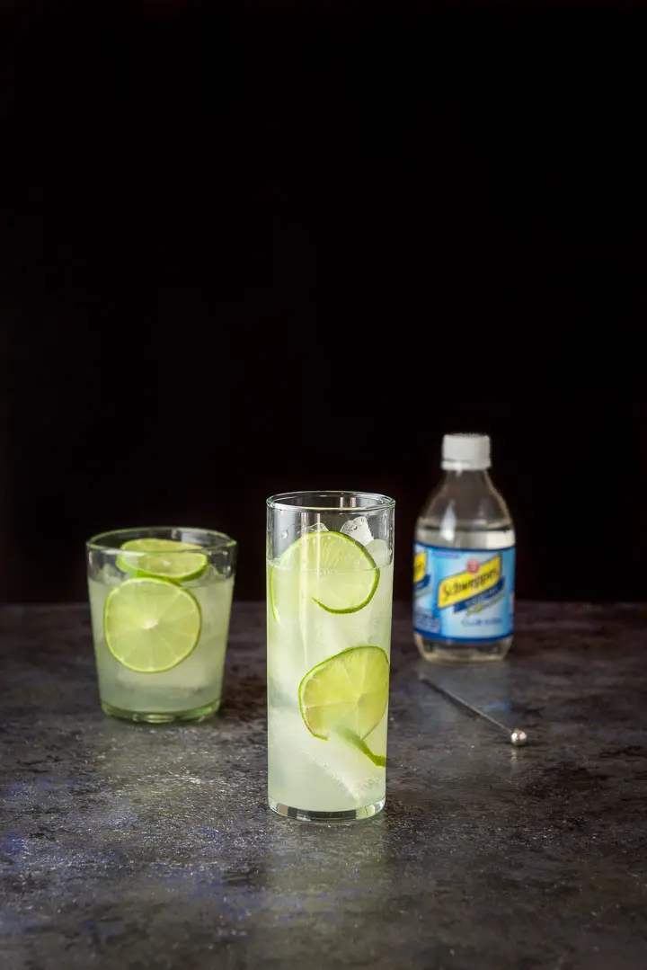 The gin and lime mixed into a glass with limes as garnish in the drink and club soda in the background