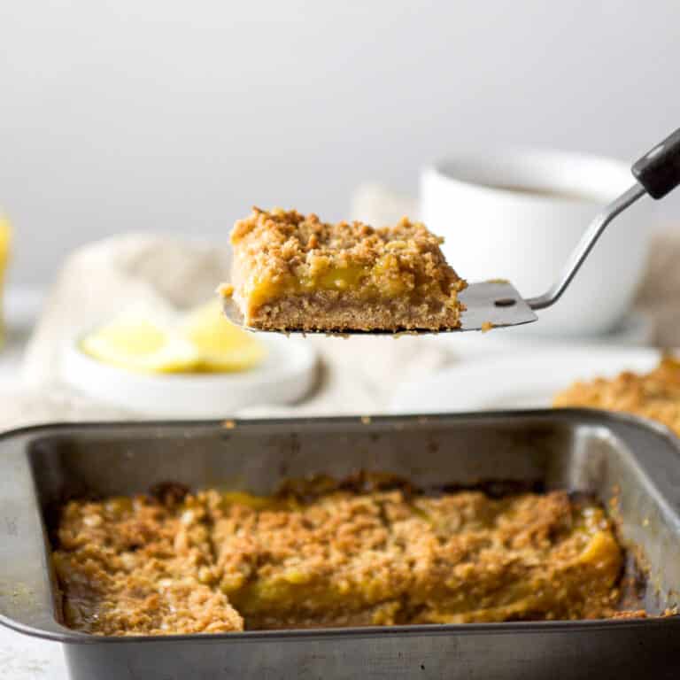 Spatula with a lemon bar on it held over a square pan with more bars in it