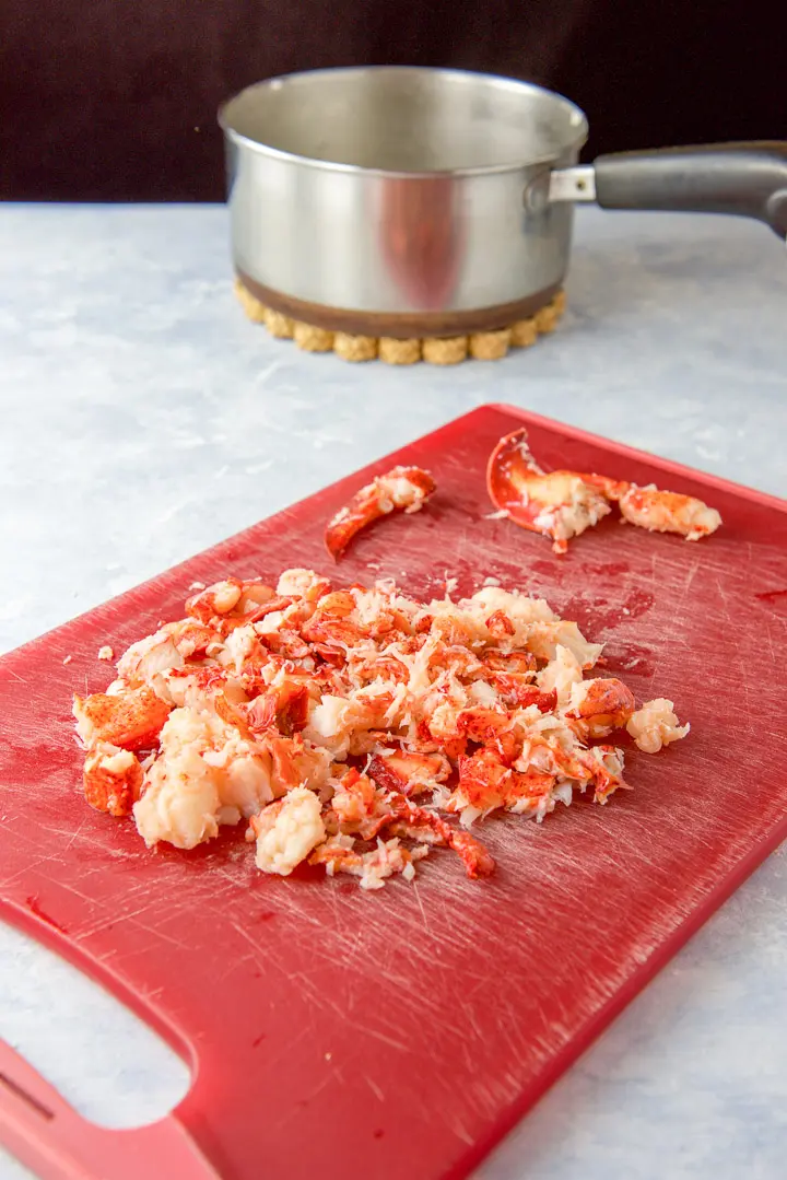 Lobster cut up on a red cutting board with a pan in the background