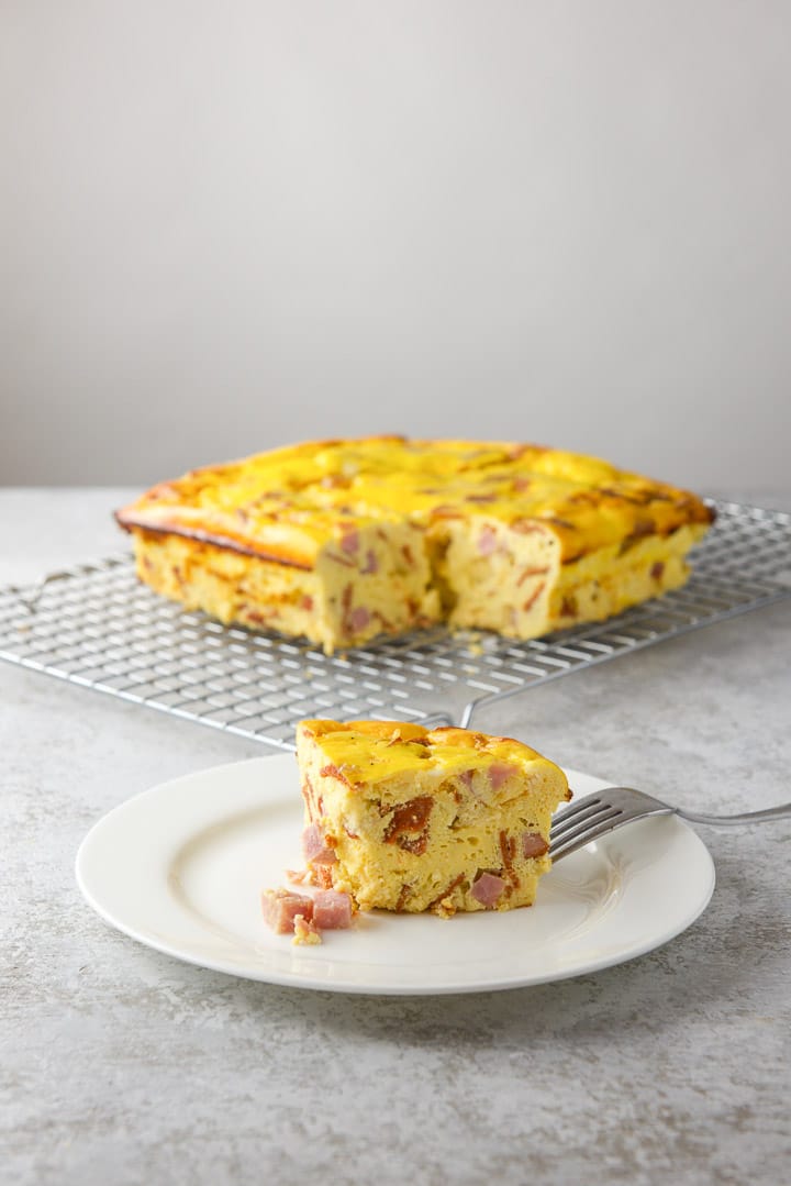 Piece of pizza gana on a salad plate, with the rest of the casserole on a cooling rack in the background.