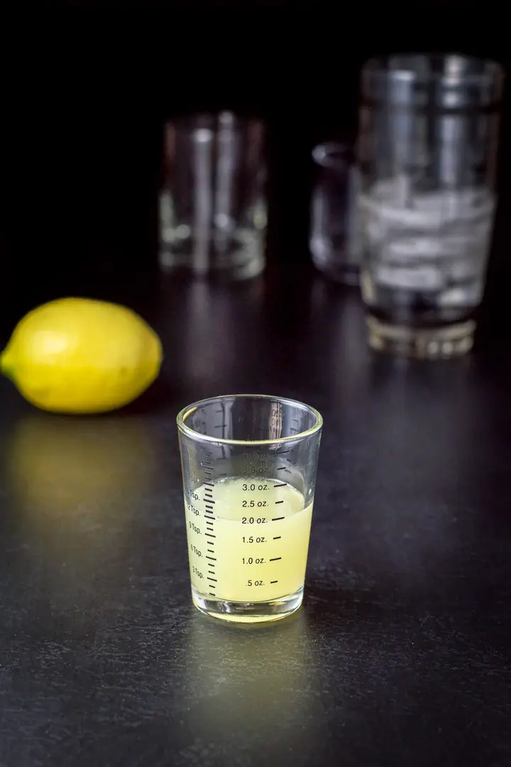 Lemon juice measured with the lemon, shaker and glassware in the background