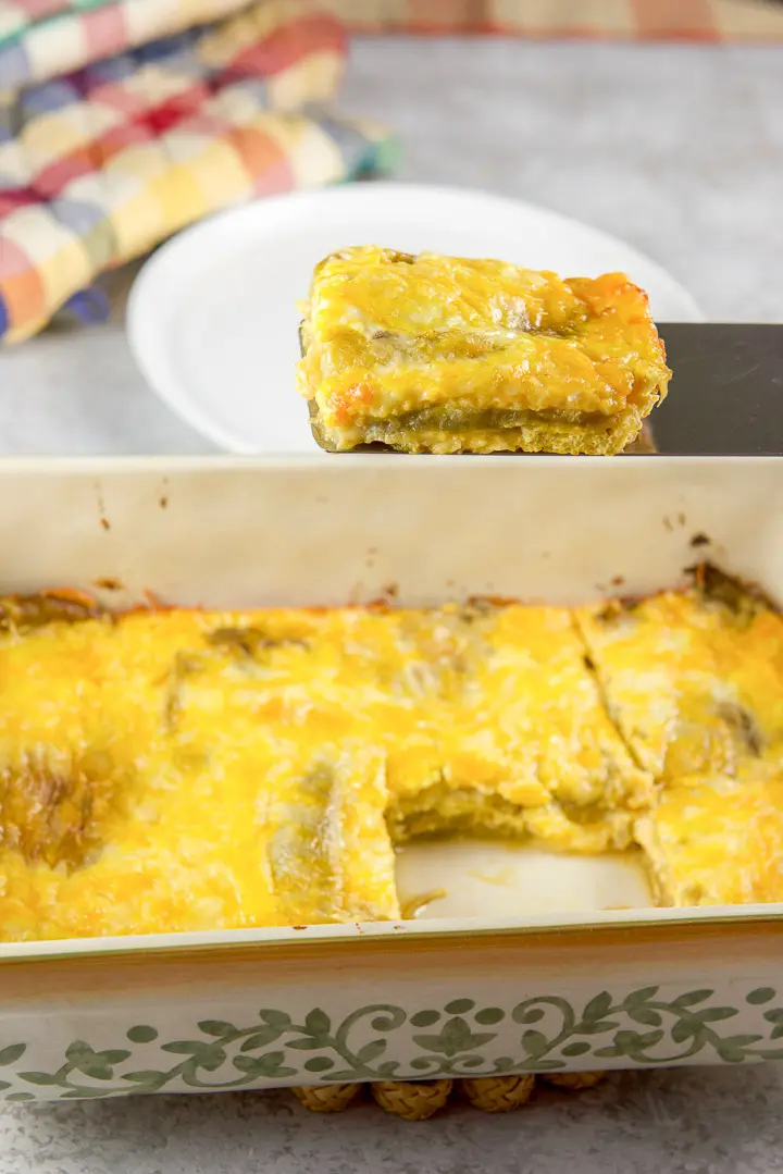 Spatula holding a piece of relleno casserole over the baking dish filled with the egg dish