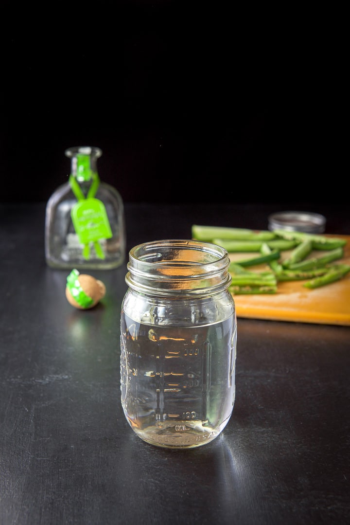 Tequila poured into a jar the the sliced jalapeños in back