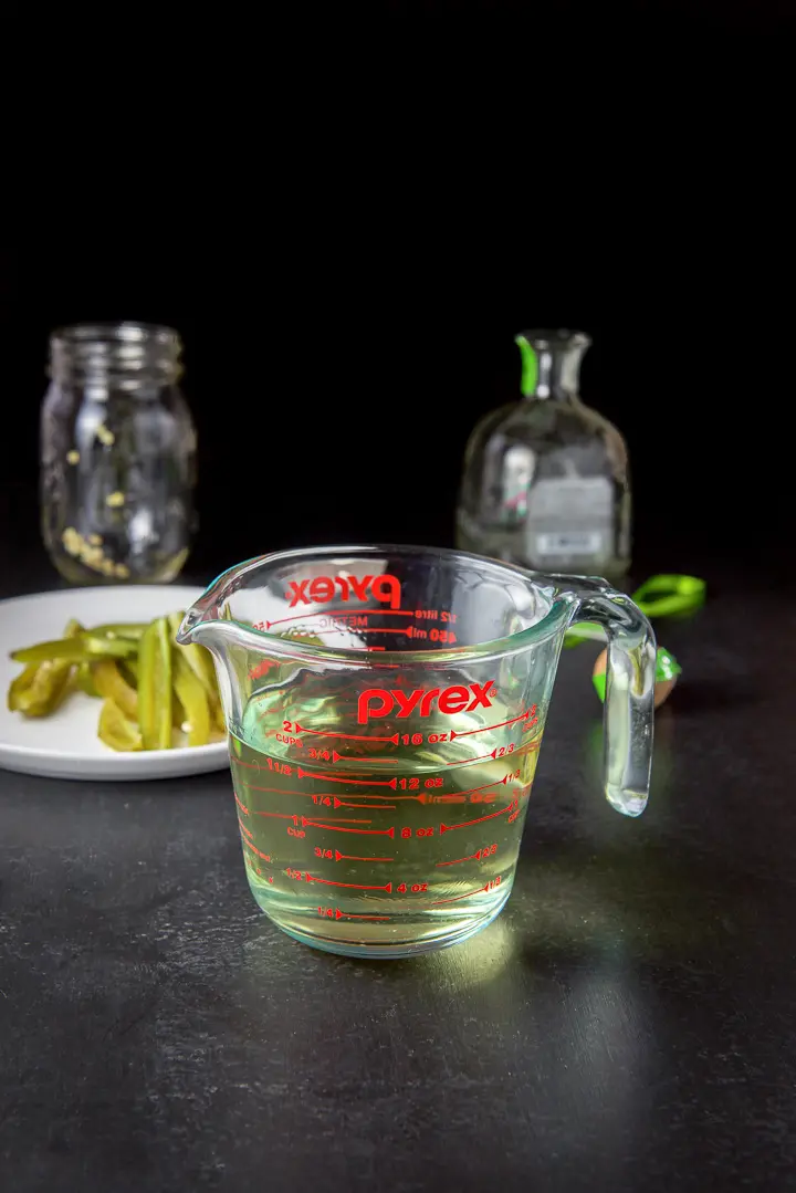 Strained infused tequila in a glass measuring cup with the jalapenos in the background