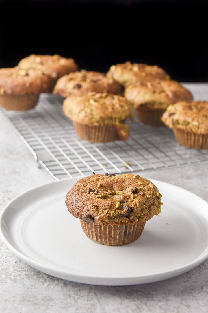 One of the pistachio filled muffins on a plate with more on the wire rack behind it