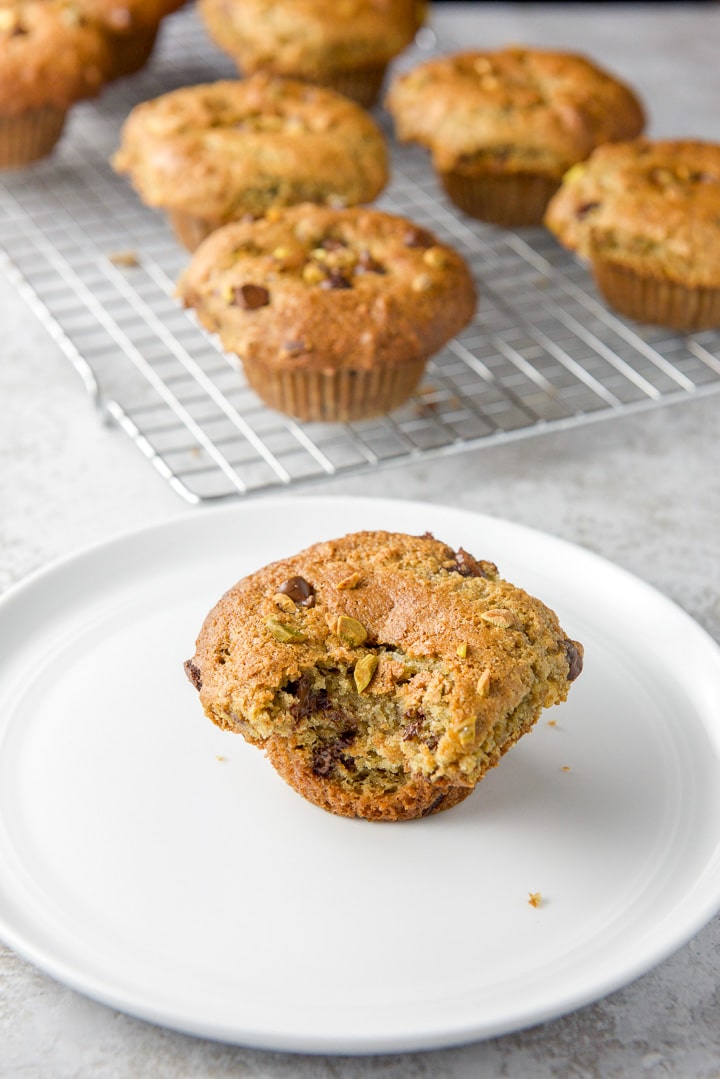 A plate with a muffin with a bite taken out of it and a wire rack with more muffins behind it