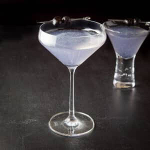 Curved glass of the purple cocktail in front of the bubble glass with the cocktail - square