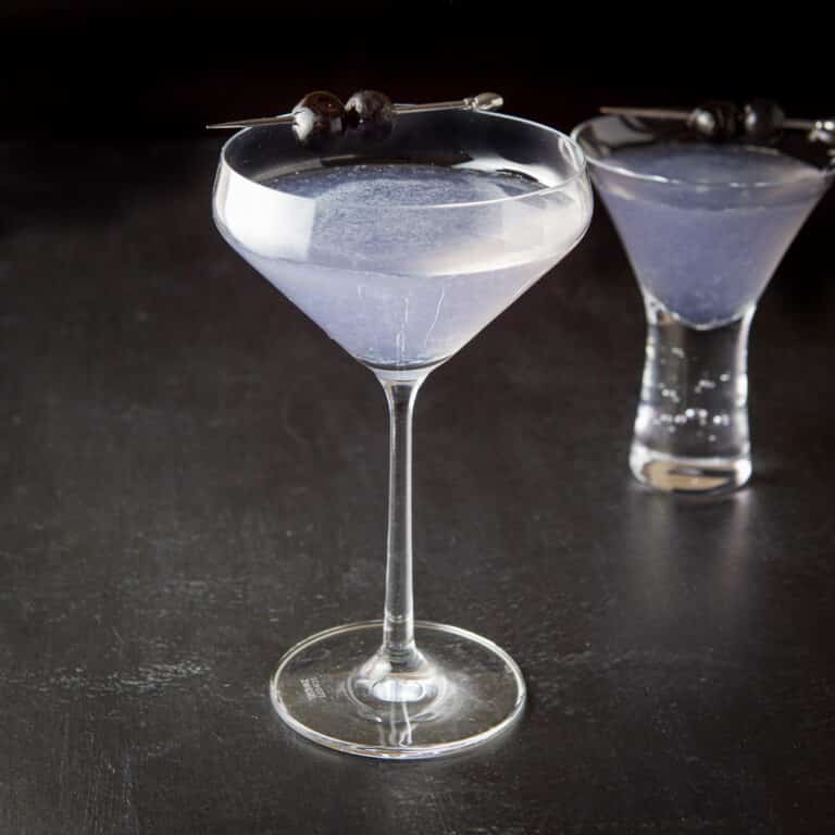 Curved glass of the purple cocktail in front of the bubble glass with the cocktail - square