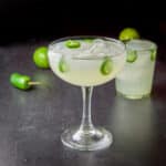 A bowl margarita glass in front of a rocks glass filled with the margarita with jalapenos in it and on the table