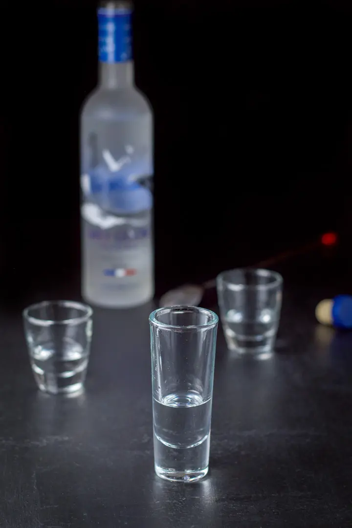 Vodka poured in three shot glasses with the bottle in the background