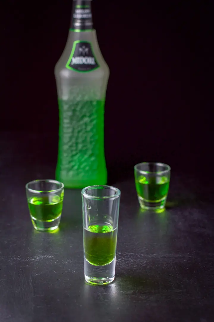 Midori layered in the three glasses with the bottle in the background