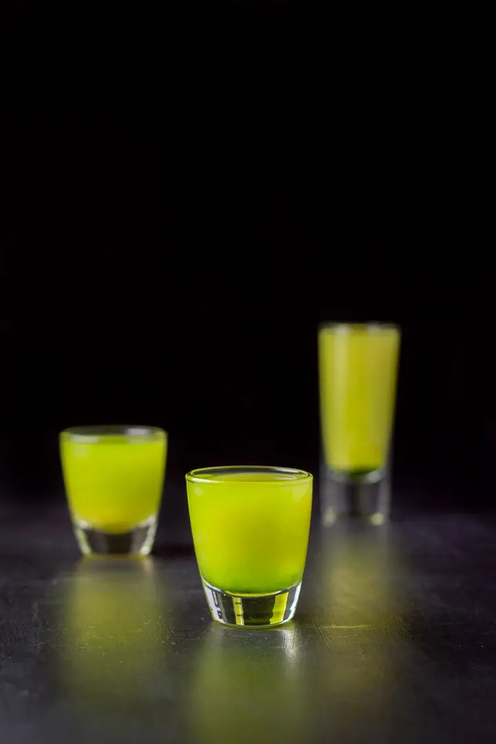 Short glass of the shot in front of the other two. You can see the Midori on the bottom with the juice at the top