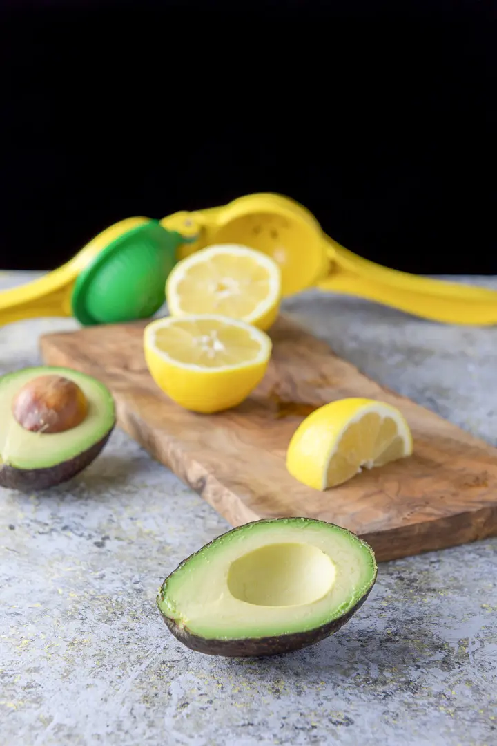 Avocado and lemons cut on a wooden board along with a citrus squeezer on the table