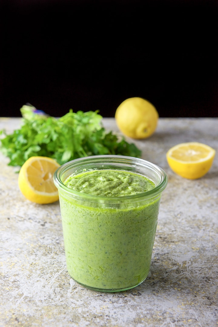 Jar filled with the avocado spread with lemons and parsley in the background