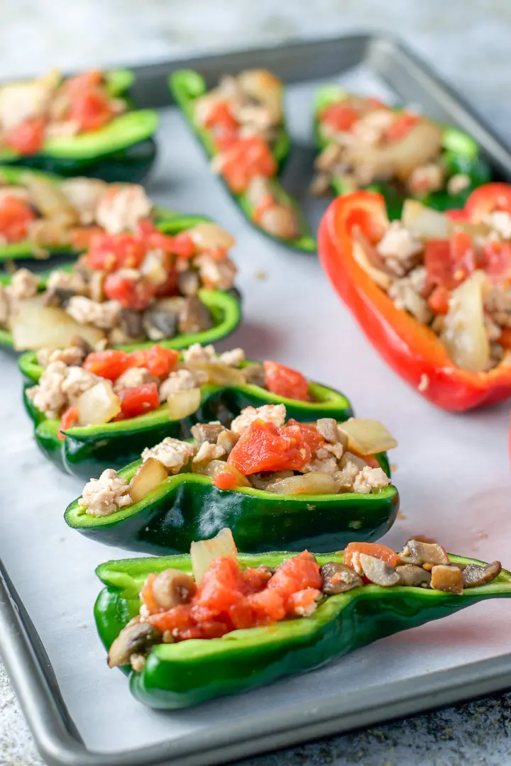 A parchment lined pan full of peppers stuffed with chicken and veggies