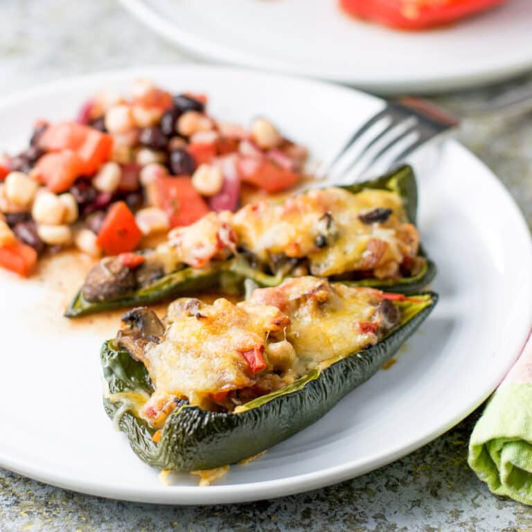 A white plate with two stuffed peppers and some bean salad - square