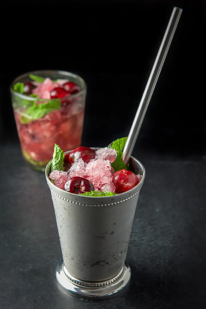 Close up of the metal cup filled with ice, cherries and bourbon. There is another glass in the background