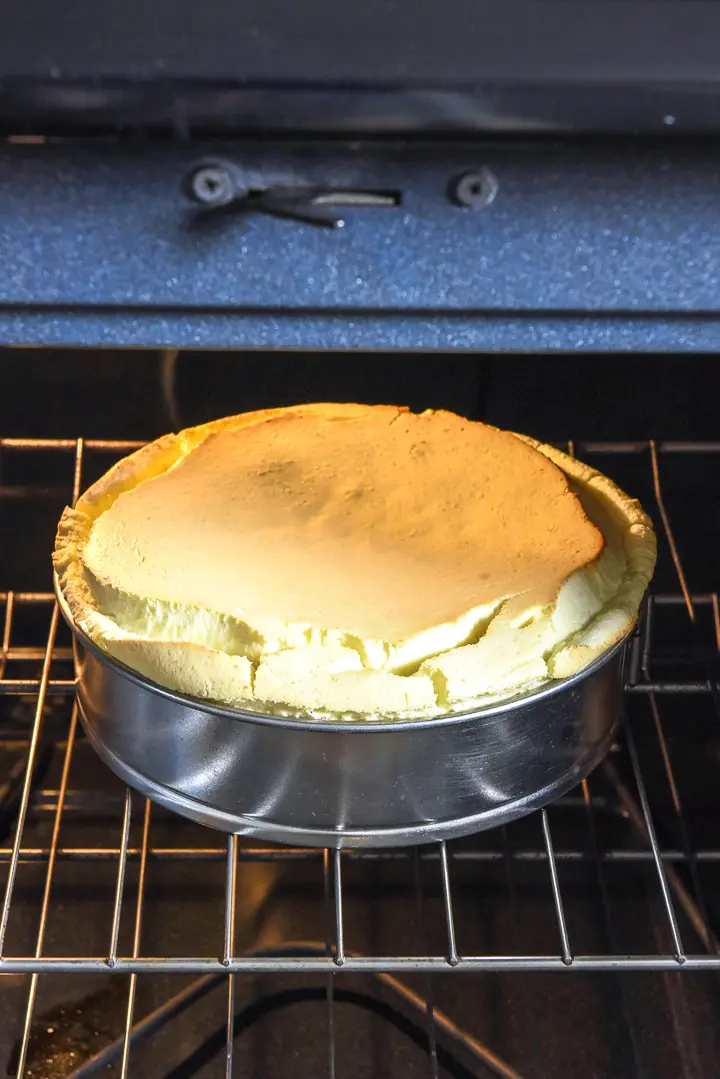 Baked cheesecake in the spring form pan, still in the oven with the door open.