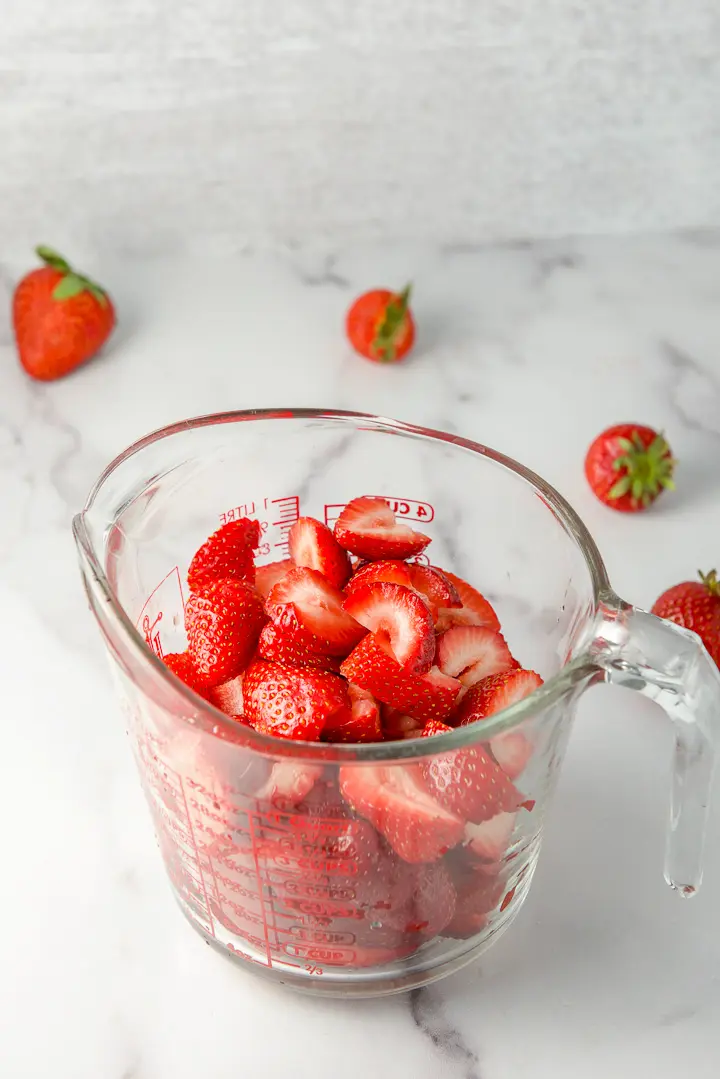 Strawberries cut up in a glass measuring cup with a few berries in the background
