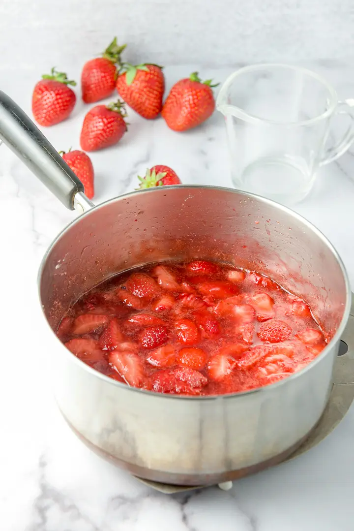 The fruit sauce cooked in the pan with strawberries in the background