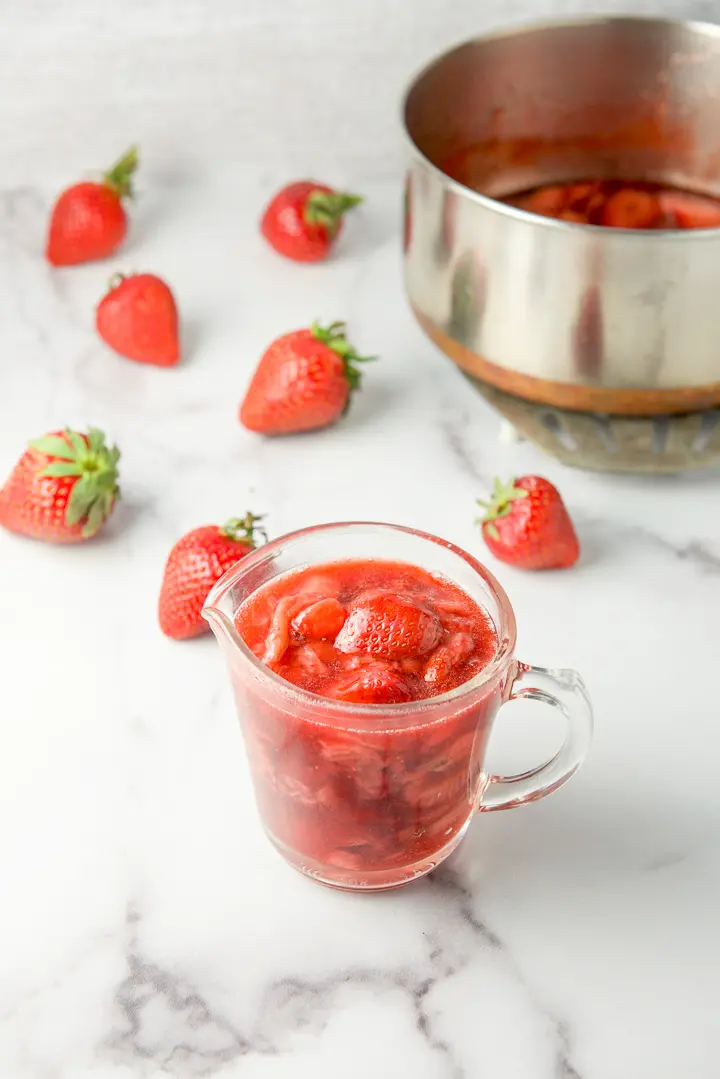 Some of the sauce in a glass pitcher with strawberries in the background