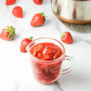 Some of the sauce in a glass pitcher with strawberries in the background