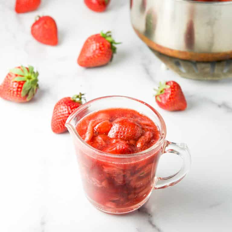 Some of the sauce in a glass pitcher with strawberries in the background