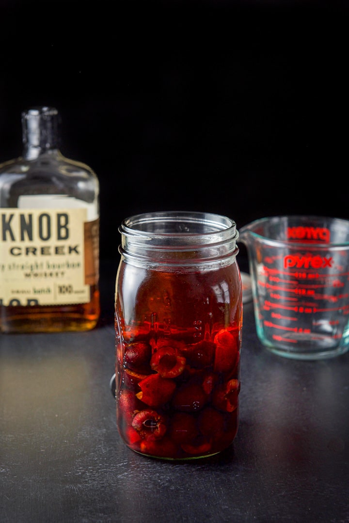 Bourbon poured into the jar to make the cherry bourbon there is a bottle of bourbon in the background
