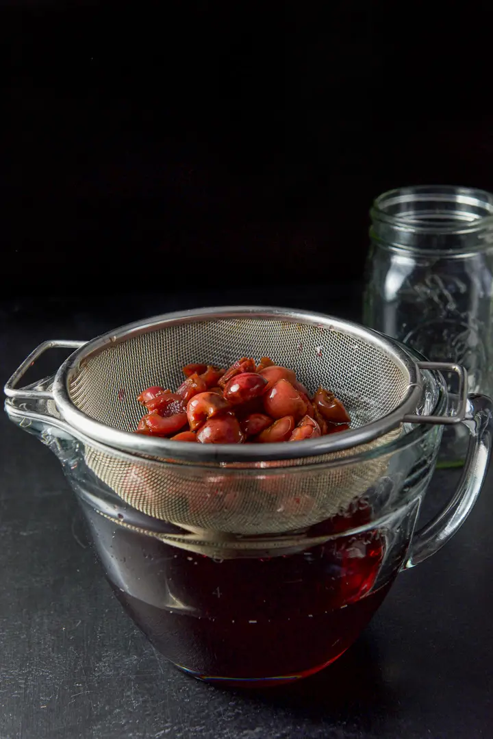 Cherries in a sieve over a bowl of the infused bourbon