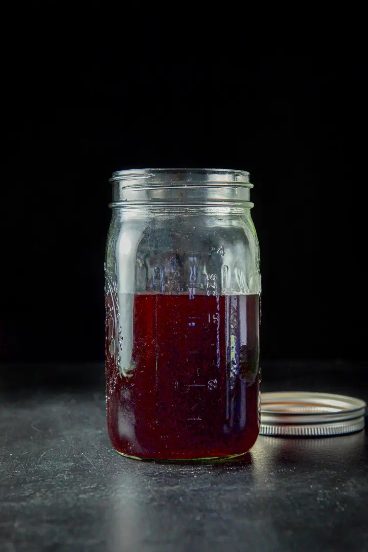 Bourbon that has been infused with cherries in a jar on a black table